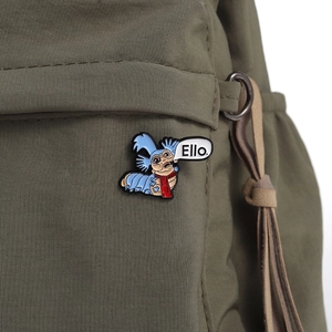 Detail showing an enamel worm pin with Ello text attached to a green canvas backpack