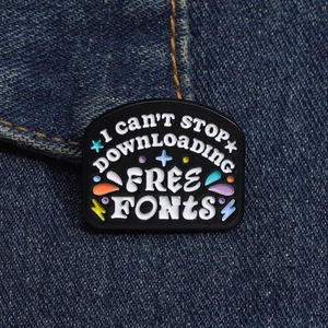 Dettaglio della spilla smaltata I CAN'T STOP DOWNLOADING FREE FONTS su una giacca di jeans