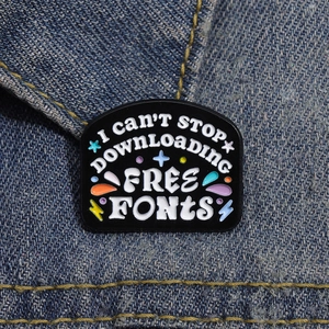 Black enamel brooch with I can't stop downloading free fonts text on denim fabric