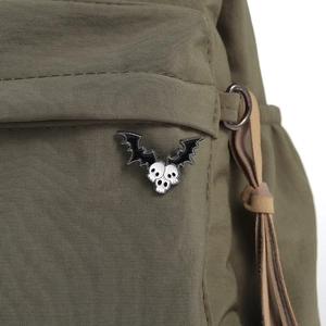 Detailed close-up of a bat-winged skull enamel pin on a green olive nylon bag