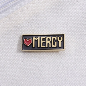 Dettaglio della spilla Mercy in smalto nero con cuore pixel rosso su fondo di tela