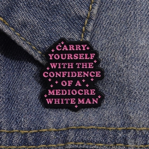Detail of creative enamel pin with pink motivational lettering on denim jacket texture