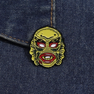 Macro shot of monster enamel pin on denim fabric showing detail of the yellow fish head mask
