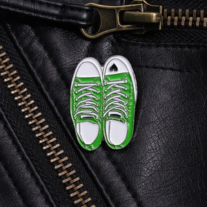 Detailed close-up of green canvas shoe enamel pins with heart detail on leather jacket