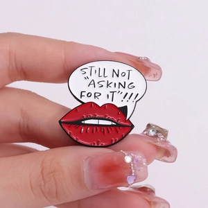 Detail of cartoon red lips alloy brooch with 'STILL NOT ASKING FOR IT' slogan
