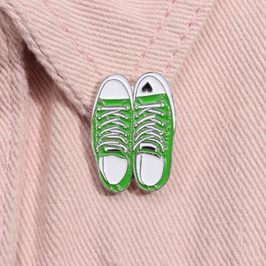 Detail of green canvas shoe enamel pins with heart detail on pink denim fabric