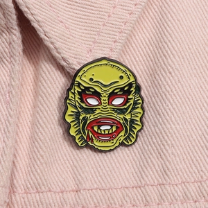Macro detail of a yellow monster enamel pin with red eyes on pink denim fabric background