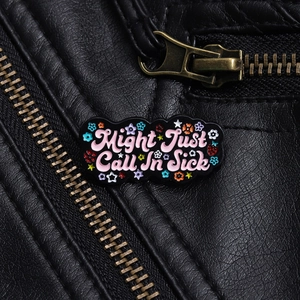 Macro detail of 'Might Just Call In Sick' enamel pin on a black leather jacket lapel