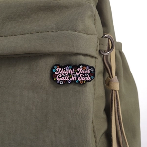 Close-up of Might Just Call In Sick enamel pin on an olive green canvas bag