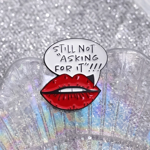 Detail of red lips enamel pin with 'STILL NOT ASKING FOR IT' quote on silver glitter