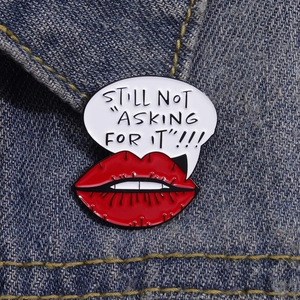 Macro shot of a red lip enamel pin with 'STILL NOT ASKING FOR IT' text on denim background