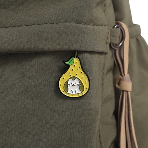 Close-up of a cartoon pear and white cat enamel brooch pinned on a green canvas bag