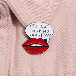 Detail of a red lip enamel pin with 'STILL NOT ASKING FOR IT' on pink denim jacket