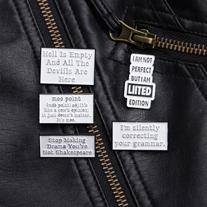 Macro shot of four white enamel alphabet pins attached to a black leather jacket texture