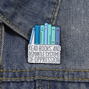 Enamel book brooch with Read Books and Dismantle Systems of Oppression quote on denim