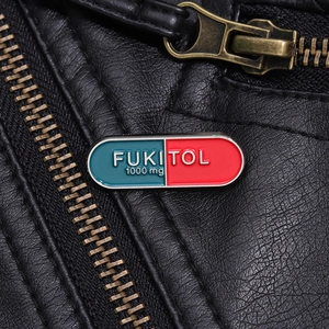 Detailed close-up of red and blue capsule enamel pin with FUKITOL text on black leather