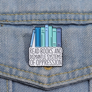 Close-up of enamel book pin with 'Read books and dismantle systems' quote on denim