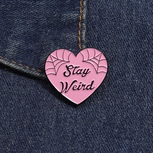 Macro shot of pink heart enamel pin with Stay Weird text on blue denim fabric background