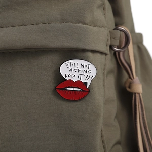 Close-up of a red lip enamel pin with speech bubble attached to a green fabric backpack