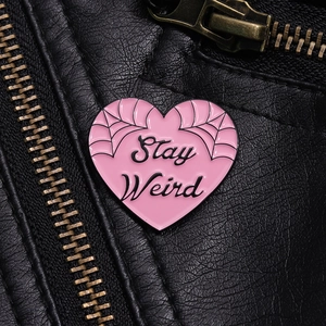 Detail of pink heart enamel pin with Stay Weird text on a black leather jacket texture