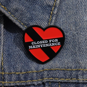 Détail d'un pin's émaillé cœur rouge et noir avec texte sur une veste en jean
