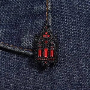 Detail of gothic church window enamel pin in black and red on dark denim fabric