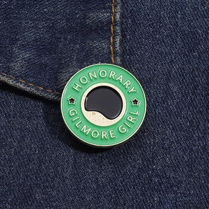 Gros plan d'une broche ronde en émail vert Gilmore Girl sur fond de tissu en denim bleu