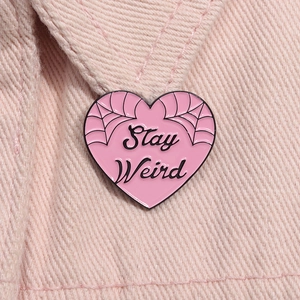 Detail of pink heart enamel pin with Stay Weird text on pink denim fabric background