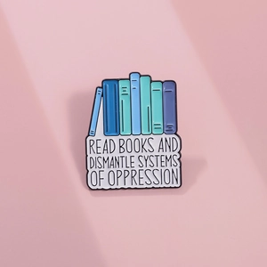 Detail of colorful book enamel pin with 'Read Books and Dismantle Systems' quote
