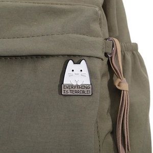 Close-up of a white cat enamel pin on a green bag with a funny slogan design