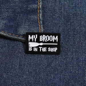 Détail d'une broche en émail noir avec texte My Broom Is In The Shop sur denim