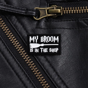 Detail of a black enamel pin with broom art on a leather jacket lapel