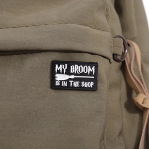 Detailed macro view of black metal badge with broom text on army green canvas fabric