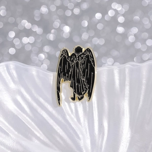 Macro shot of an enamel angel brooch with black wings on a white textured shell