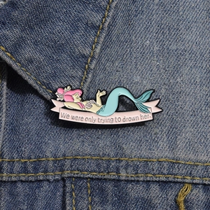 Détail d'un pin's sirène en émail sur veste en jean avec citation et dessin animé