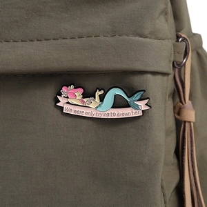 Détail d'un pin's sirène en émail rose attaché sur un sac en toile vert militaire