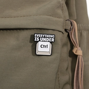 Detail of Control key enamel pin with 'Everything is under' text on green fabric