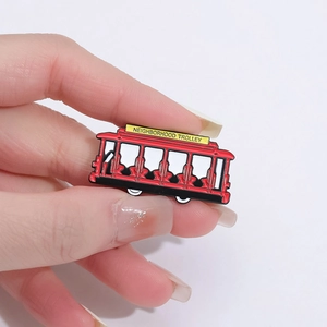 Detailed macro view of the red enamel Neighborhood Trolley lapel pin held by fingers
