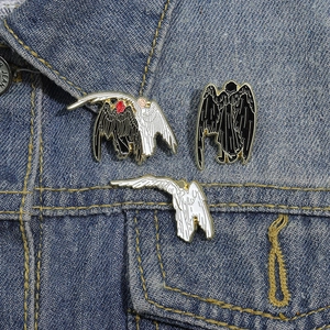 Three angel enamel pins with black and white wings on a blue denim jacket collar