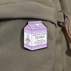 Detail of creative purple milk carton enamel pin with Chemistry Student Tears text on fabric