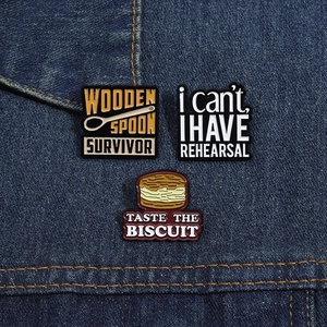 Close-up of three enamel pins with quotes and biscuit design on denim fabric