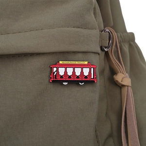 Detailed close-up of a red enamel Neighborhood Trolley pin on a green canvas bag