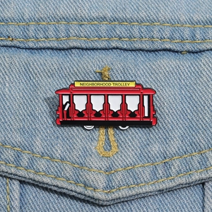 Close-up of a red Neighborhood Trolley enamel pin on blue denim fabric background