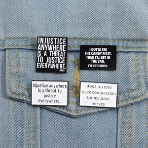 Détail de quatre pins rectangulaires en émail avec citations anglaises sur veste denim