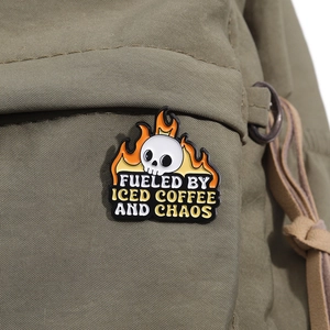 Detail of cartoon skull enamel pin on canvas bag fueled by iced coffee and chaos