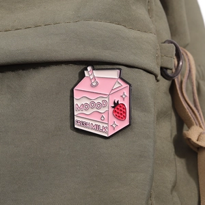 Detail showing pink strawberry milk carton enamel pin on green canvas bag