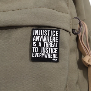Détail d'une épingle en émail noir avec citation de MLK sur un sac à dos en toile verte