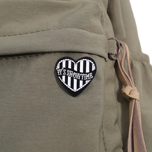 Detail of heart enamel pin with black and white stripes on a green backpack strap