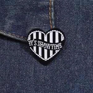 Detail view of a heart-shaped enamel pin with black and white stripes and text on denim fabric