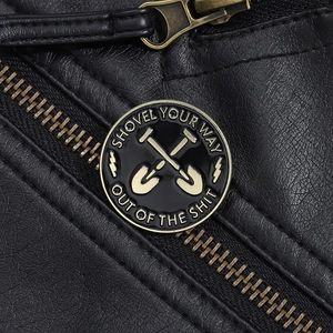 Macro shot of an enamel metal pin badge on black leather featuring a shovel design
